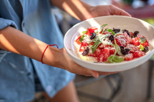 Persona sosteniendo un bol con ensalada de sandía, queso y rúcula al aire libre