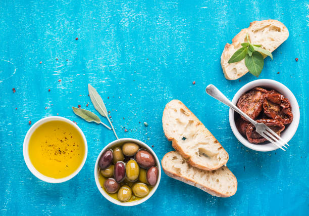 Aceite de oliva, aceitunas, pan y tomate seco sobre fondo azul